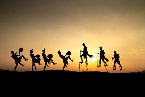 Free Silhouettes of performers with drums and stilts against a vibrant sunset sky, capturing a dynamic scene. Stock Photo