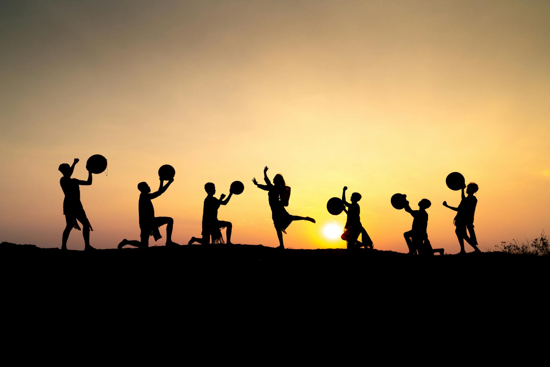 Silhouette of people joyfully performing with drums against a stunning sunset backdrop.