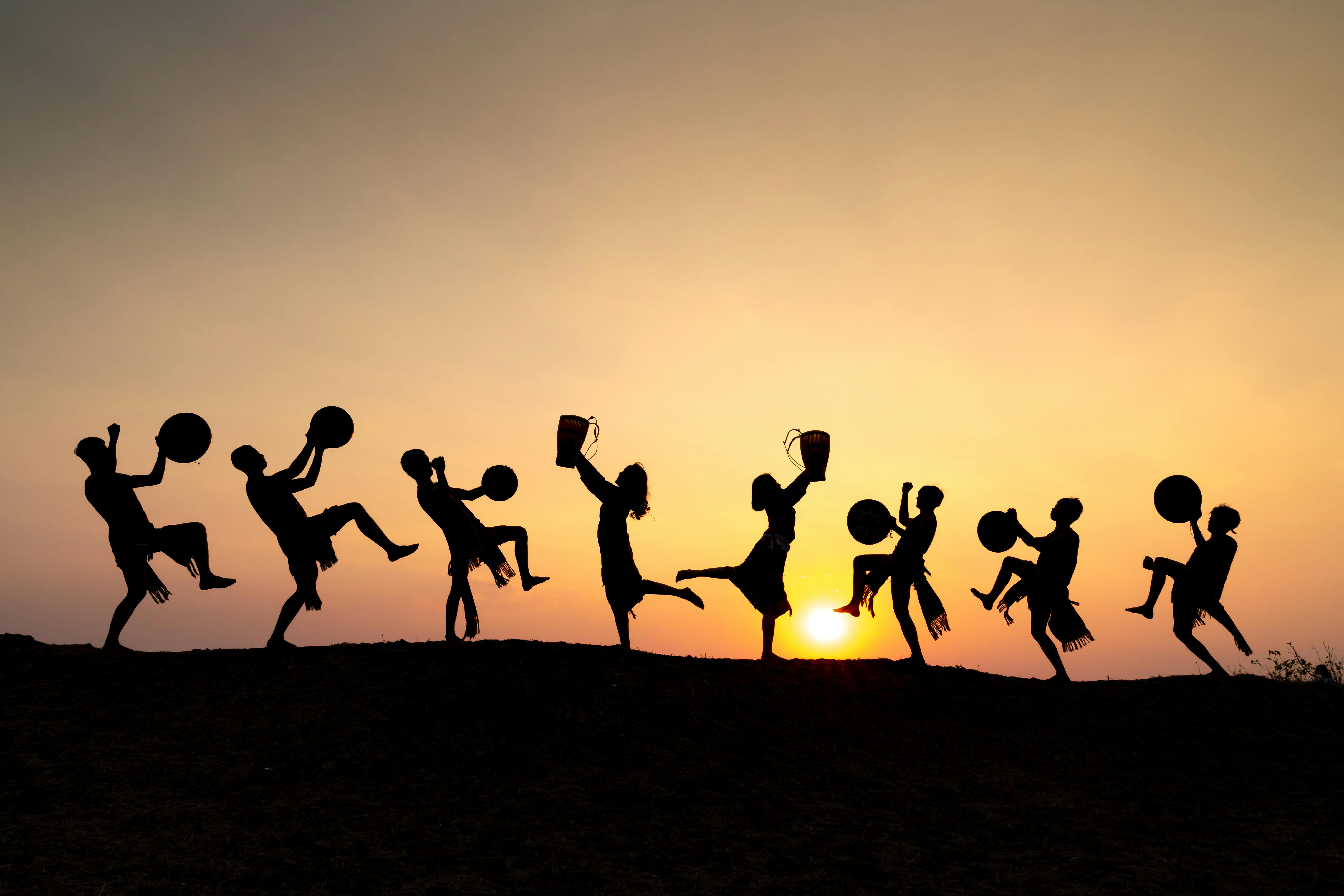 Dancers with drums silhouette against a vibrant sunset sky, showcasing rhythm and joy.