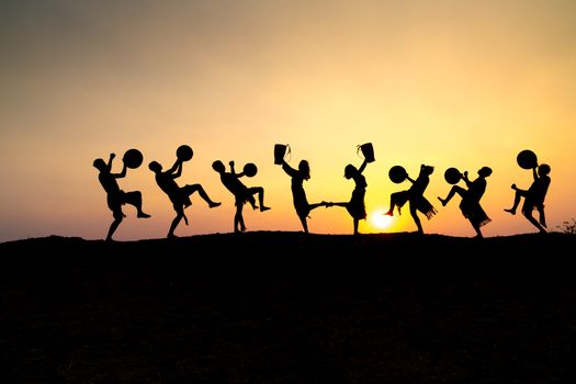 Silhouettes of people dancing with drums against a vibrant sunset.