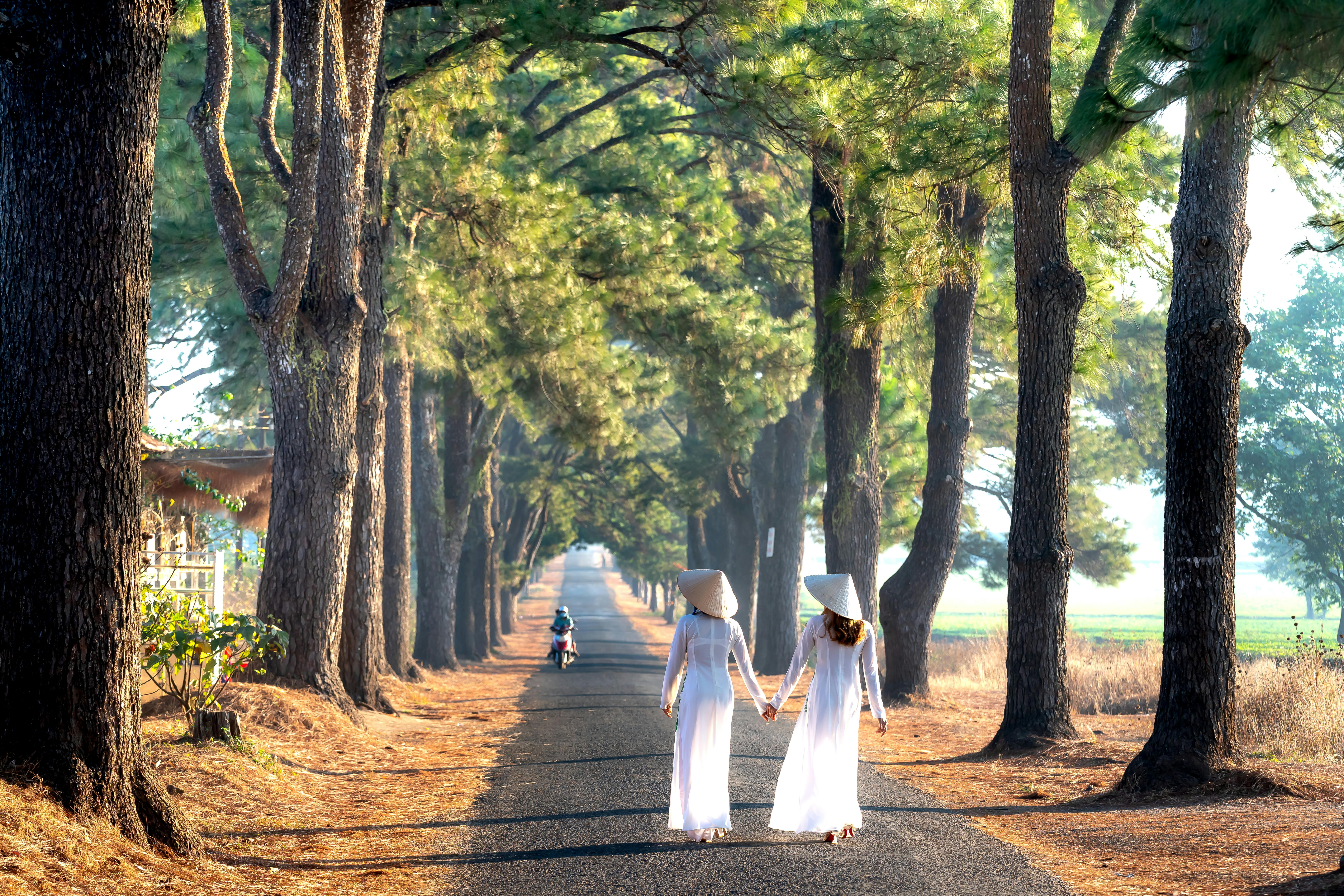 women in white ao dai strolling in park holding han