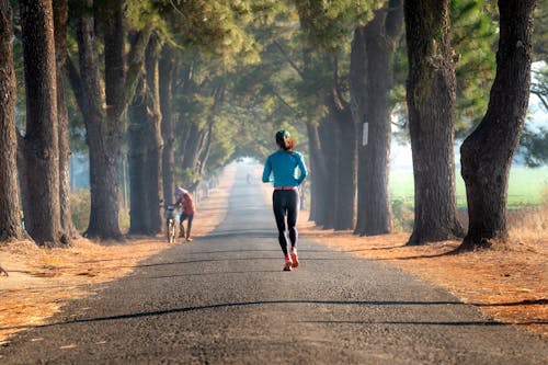 A Back View of a Woman in Black Leggings Running on a Concrete Road