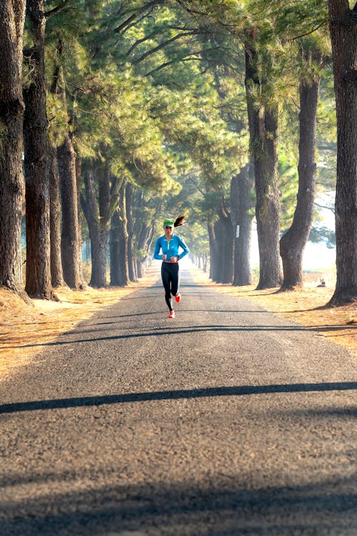 A Woman in Blue Long Sleeves Running Between Green Trees