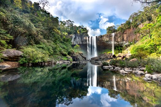 A stunning waterfall surrounded by lush greenery, reflecting in a calm river.