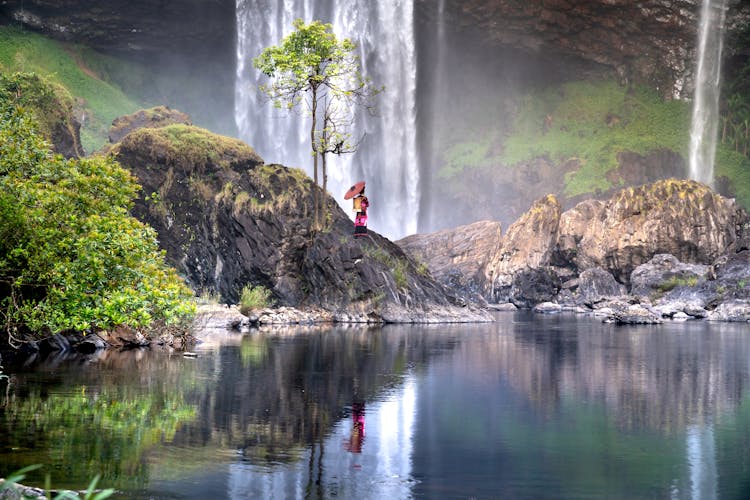 Woman In Traditional Clothes Near Waterfall In Nature