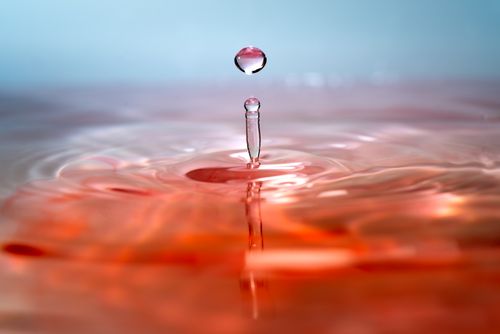 Free Artistic macro shot capturing a water droplet splash with reflection on a red surface. Stock Photo