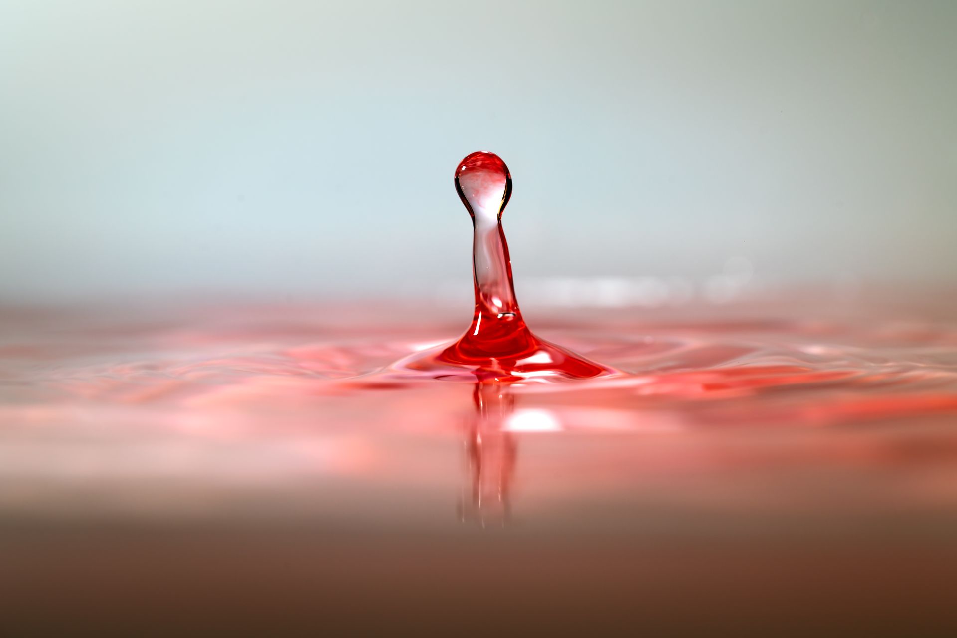 Close-up image of a red water droplet creating ripples, captured in motion with selective focus.
