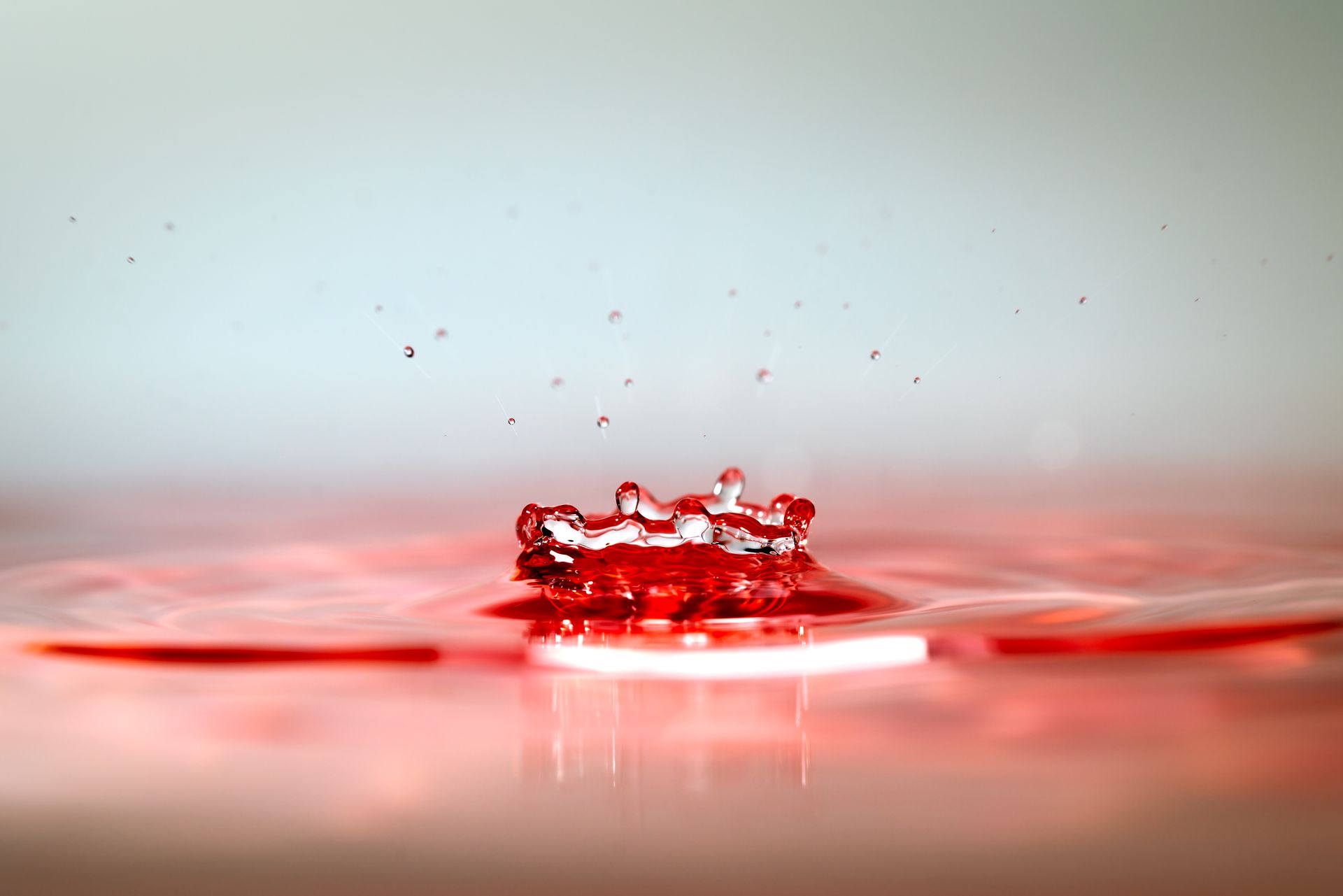 Close-up photo of a red water droplet creating ripples, showcasing fluid dynamics.
