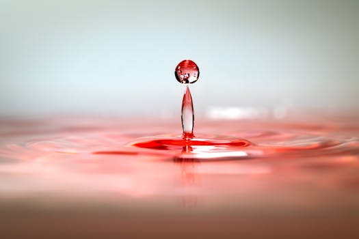 Dynamic close-up of a red water droplet captured in motion with ripples on the surface.
