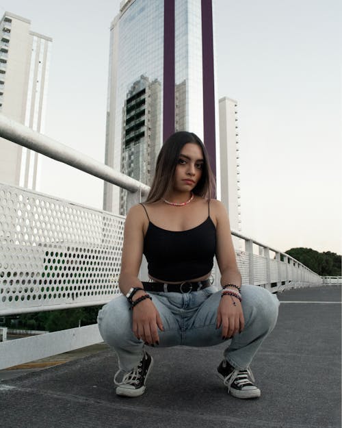Woman in Black Tank Top and Blue Denim Jeans Squatting on the Ground