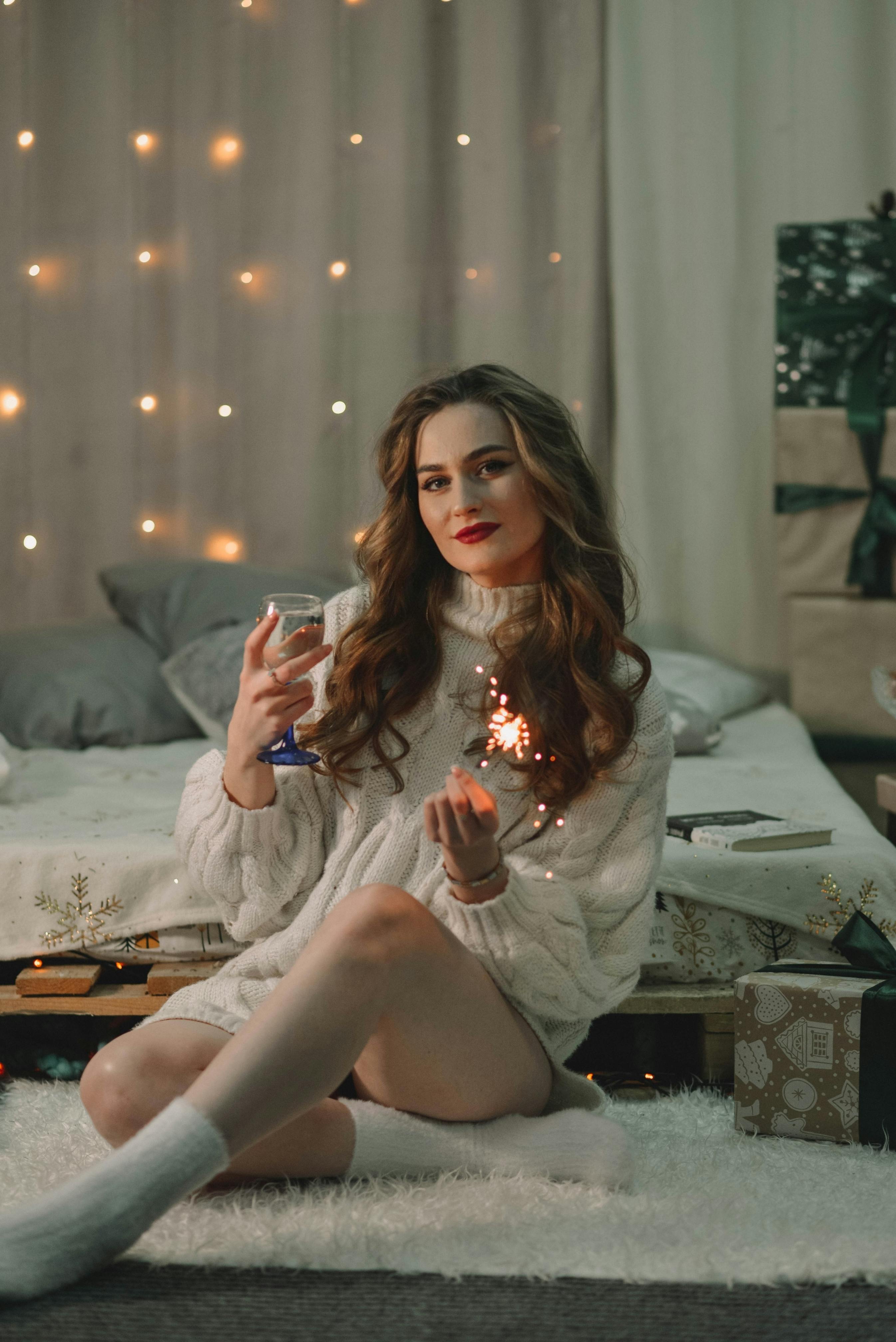 woman holding champagne and sparkler sitting on floor in sweater