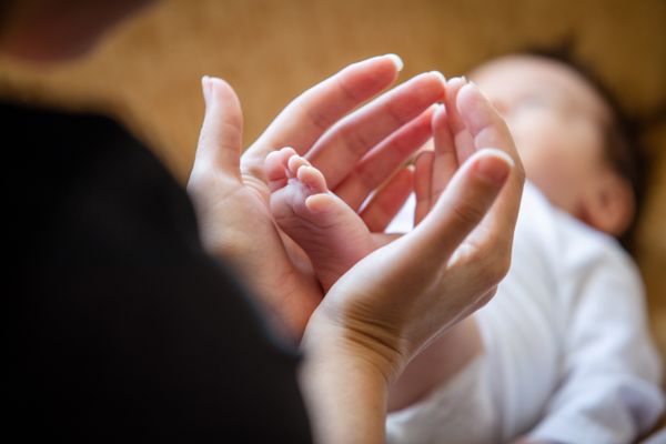 A mother's hands gently holding her newborn baby's feet