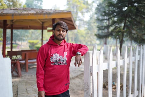 Man in Red Hoodie Standing Beside Wooden Fence