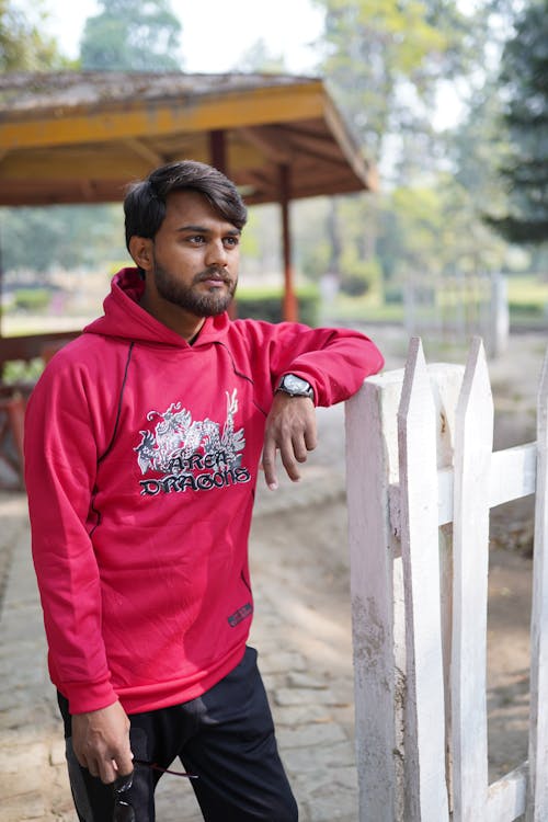 Man in Red Hoodie Standing Near White Wooden Fence