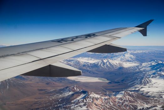 Spectacular aerial view of snow-capped mountains seen from an airplane wing.
