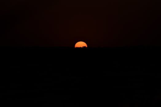 A captivating sunset with an orange sun setting against a dark horizon, creating a mysterious ambiance.