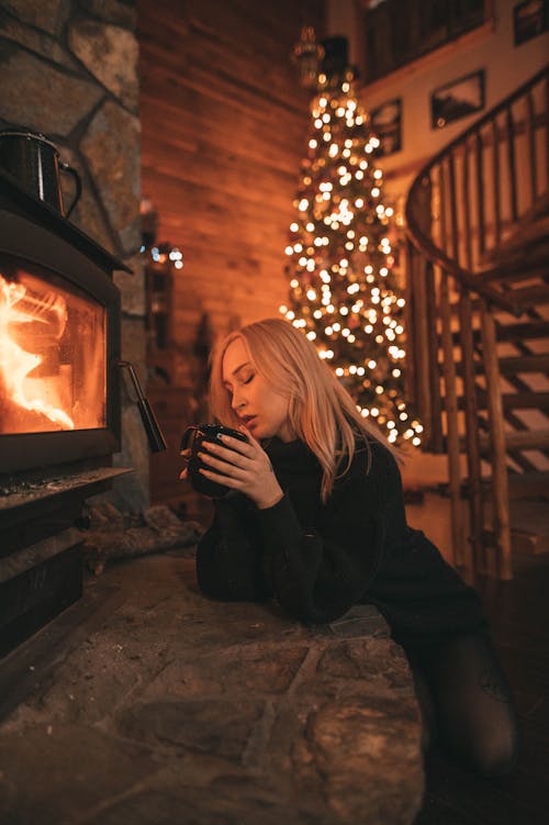 Free Woman Sitting by Fireplace Holding Cup Stock Photo