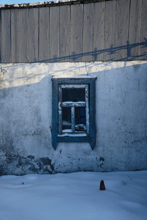 Free A weathered blue wooden window on a snow-covered rustic wall, casting shadows. Stock Photo
