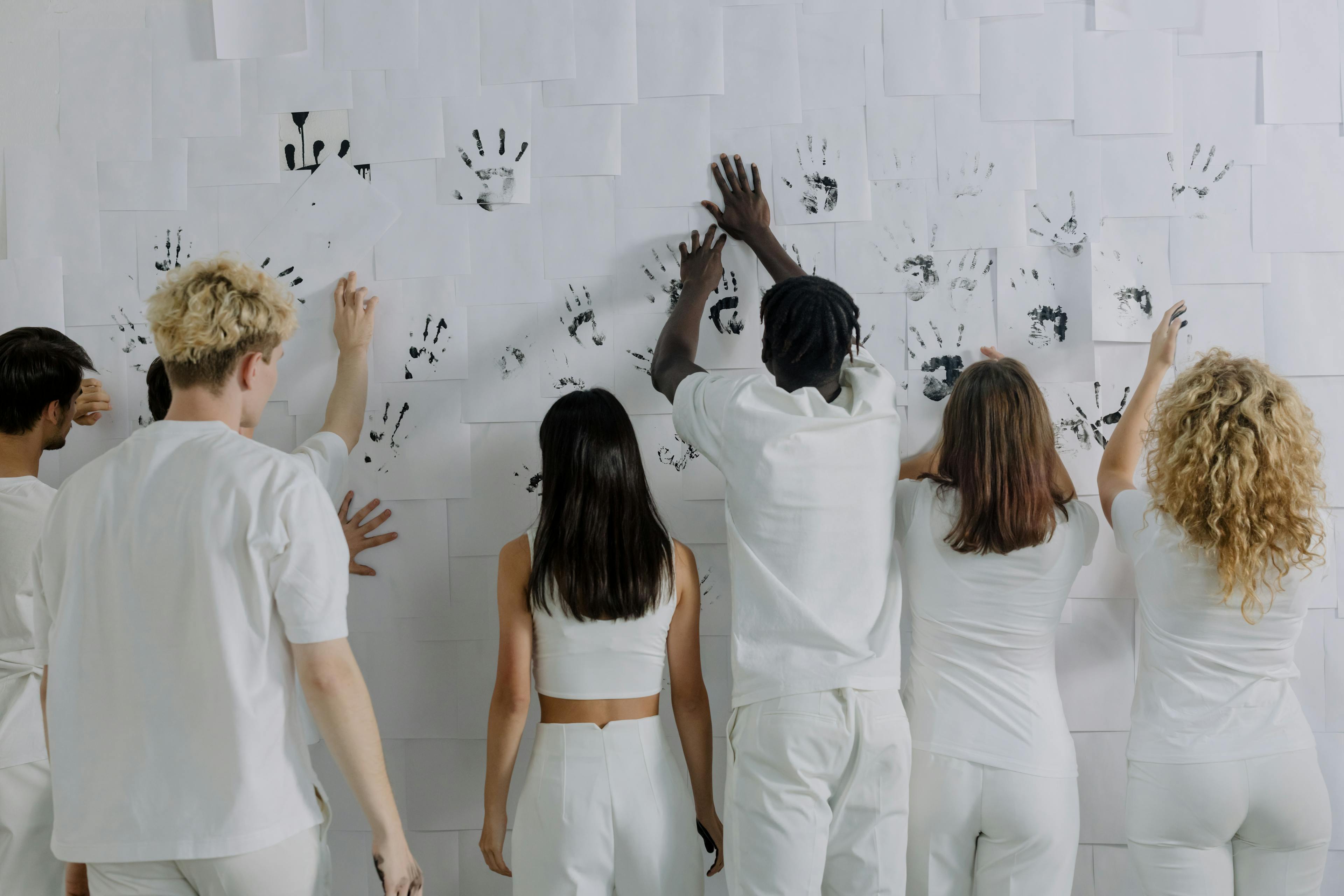A diverse group of people imprinting handprints on a white wall, symbolizing unity and equality.