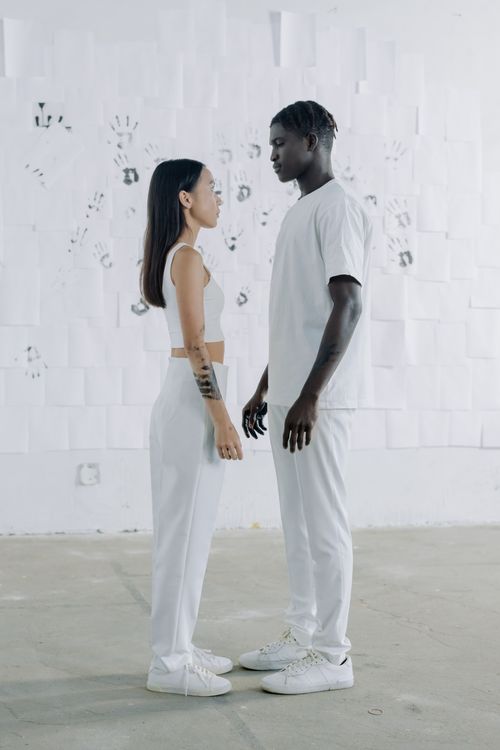 Free Interracial couple standing face to face wearing white in a minimalist setting. Stock Photo