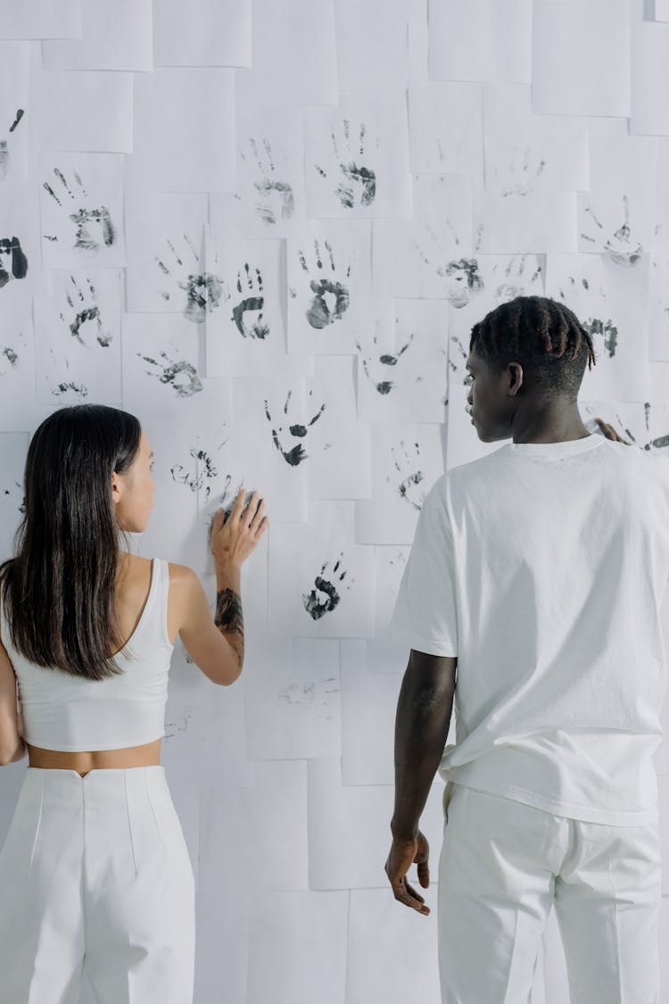 A Man And A Woman In White Clothes Marking Their Hands On Papers Posted On A Wall