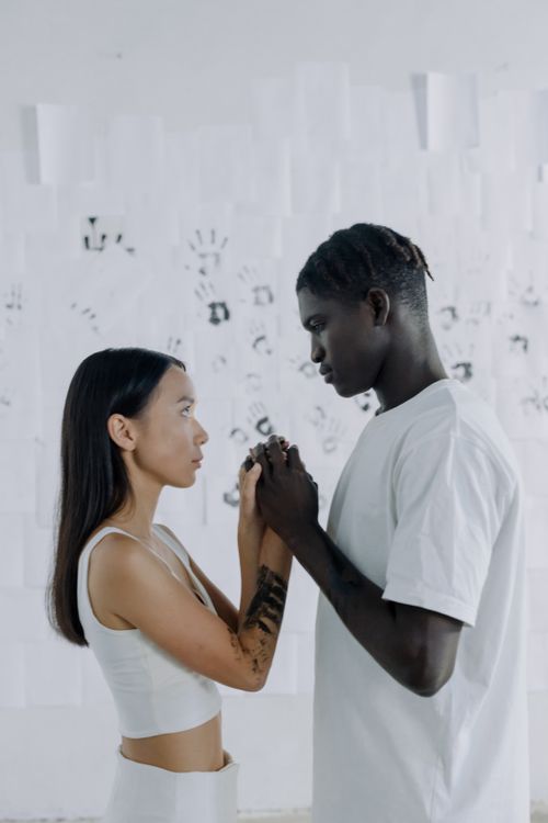 Free A black man and asian woman holding hands in an artistic setting, symbolizing unity. Stock Photo