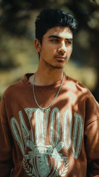 Portrait of a young man wearing a brown Oakwood sweatshirt outdoors in soft, natural light.