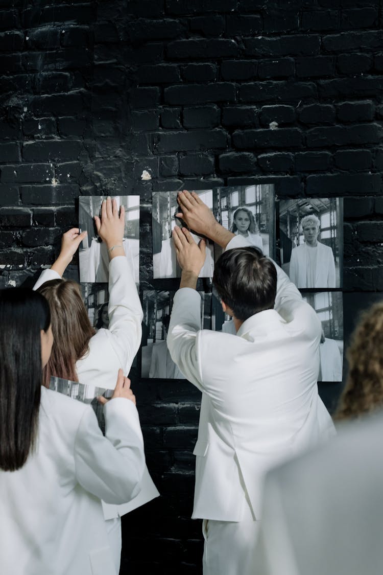 People In White Suits Hanging Black And White Photos On A Wall 