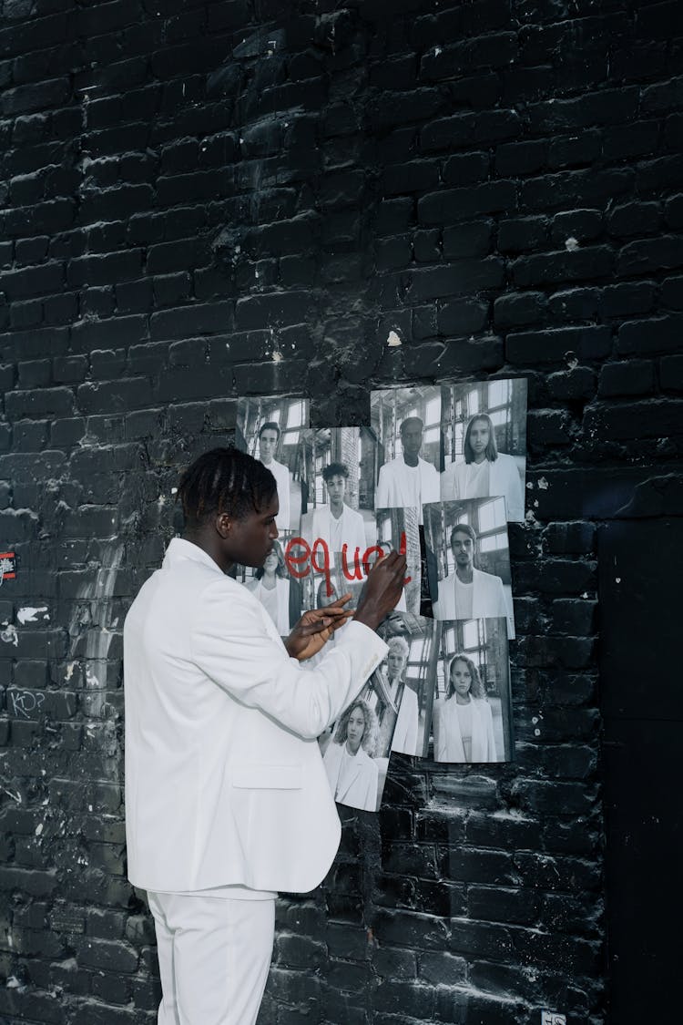 A Man In White Clothes Writing The Word Equal On Pictures Of People Posted On Wall