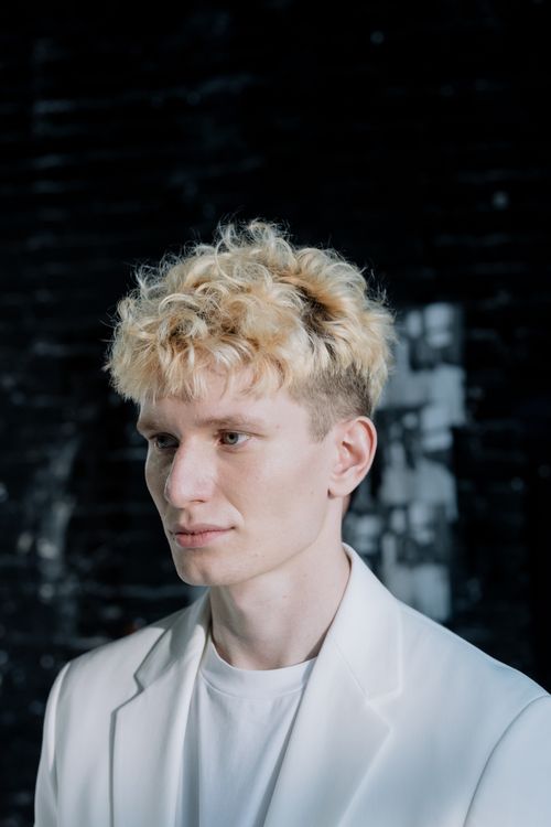 Free Portrait of a young man with blonde curly hair against a dark background. Stock Photo