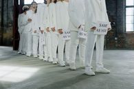A group of individuals in white suits holding 'Same as You' signs, symbolizing unity and conformity.