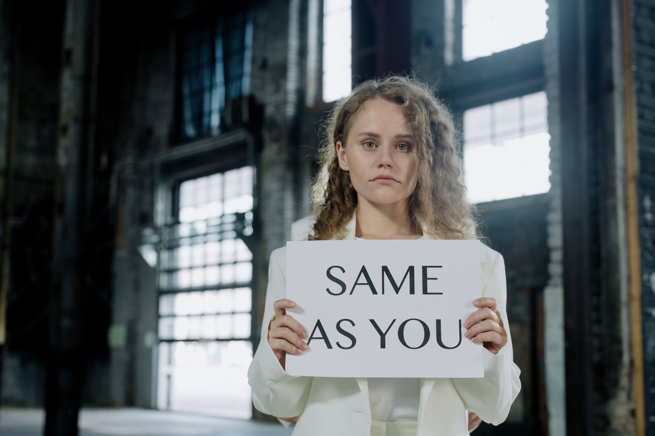Caucasian woman in white outfit holding sign with text in urban setting.
