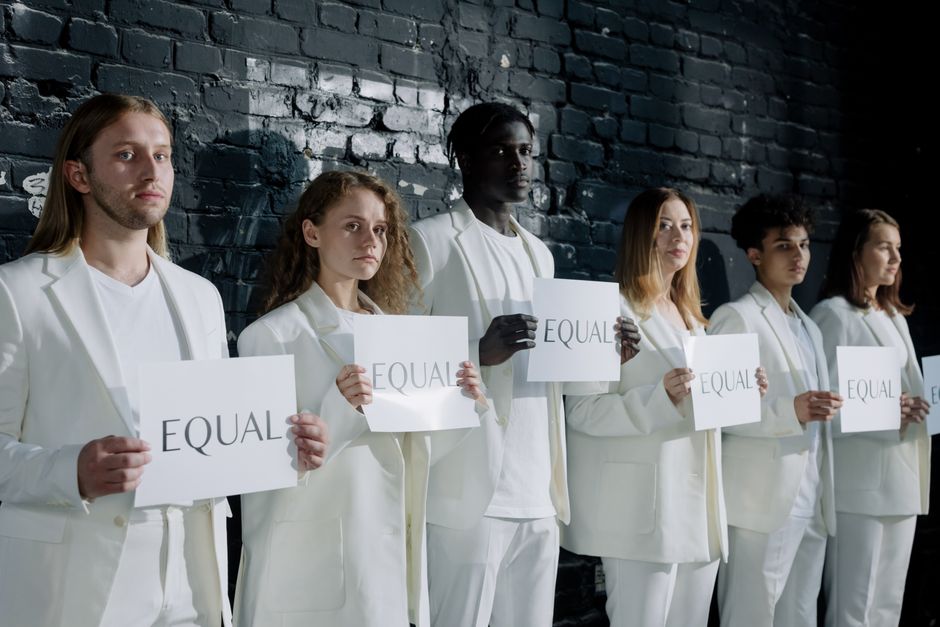 Un grupo diverso de personas en vestimenta blanca sosteniendo carteles que dicen 'Igual', promoviendo la igualdad.