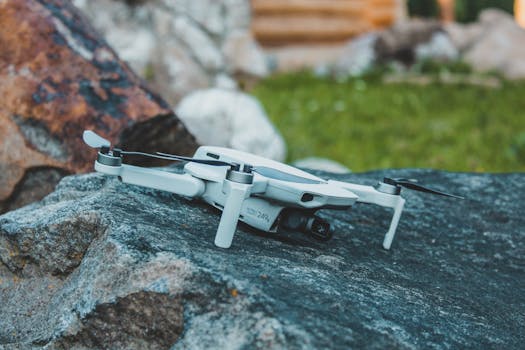 A sleek white compact drone resting on a rock outdoors, showcasing its design and portability.
