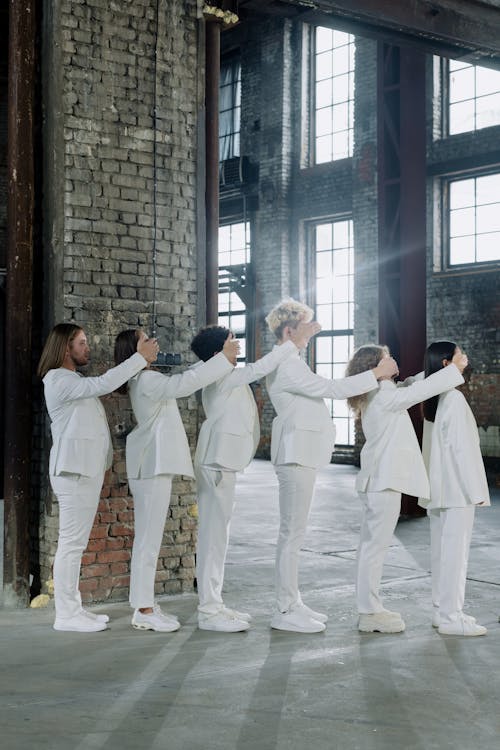 Group of People in White Clothes Standing in a Line and Covering Eyes of the Person in front of Them 