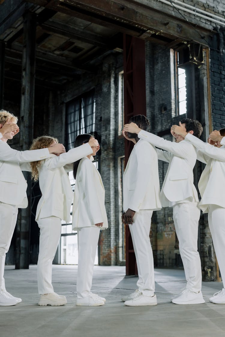 A Group Of People In White Uniform Covering The Eyes Of The Person In Front