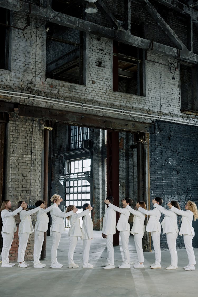 A Group Of People In White Uniform Covering The Eyes Of The Person In Front