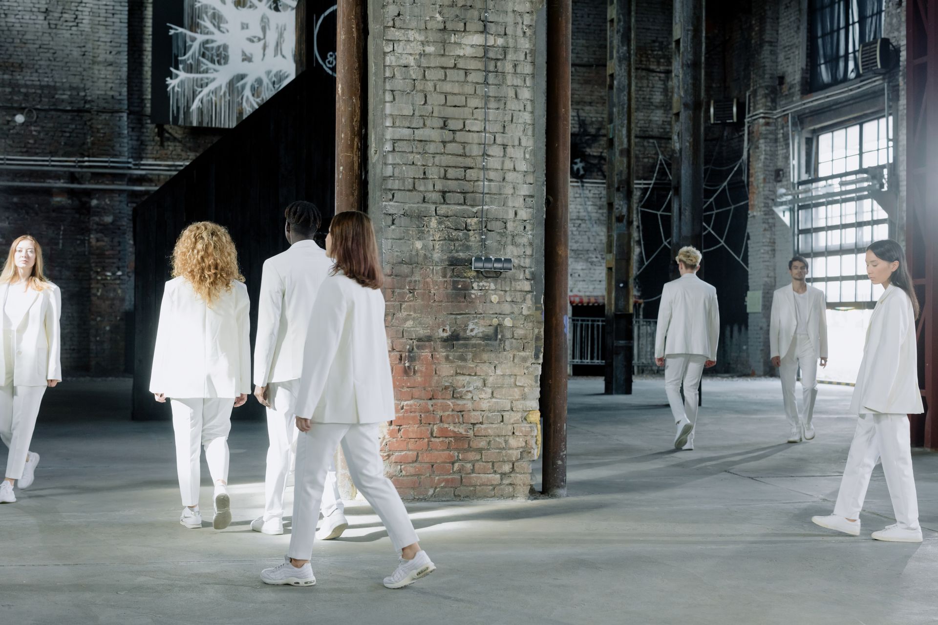Group of fashionably dressed adults in white suits walking inside an urban industrial space.