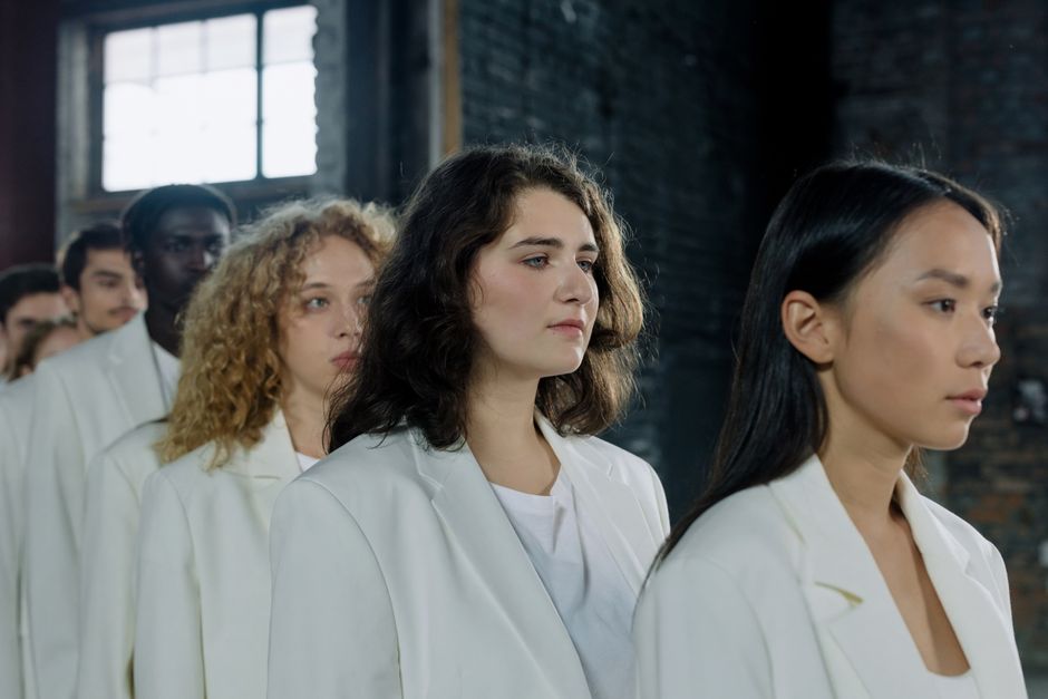 A diverse group of people standing in line indoors, wearing white outfits, with a focus on unity and harmony.