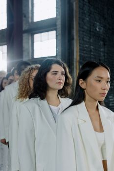 A group of diverse women standing indoors wearing white outfits, creating an artistic concept.