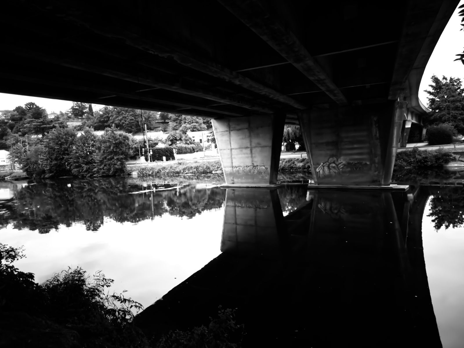 Pont routier en béton reflété dans une rivière calme, en noir et blanc