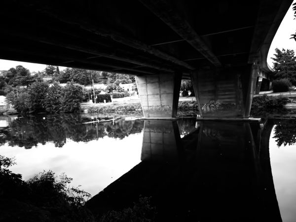 Pont routier en béton reflété dans une rivière calme, en noir et blanc
