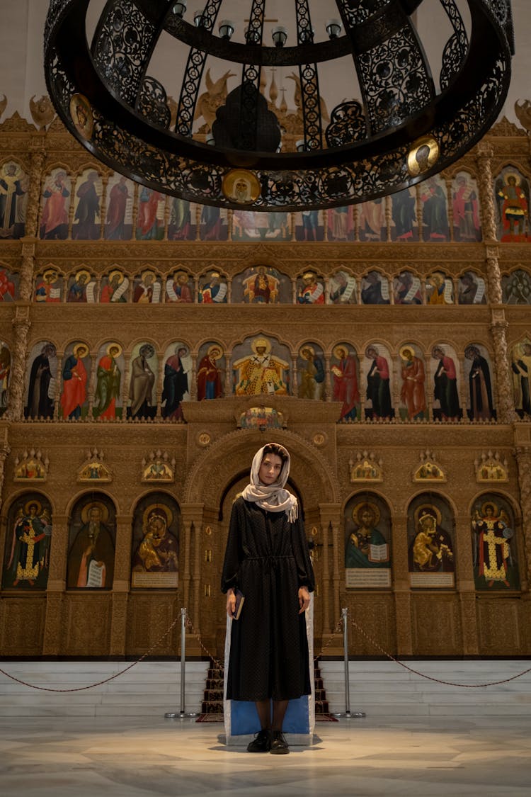 Woman Standing In Church Under Black Chandelier Pending From Vault