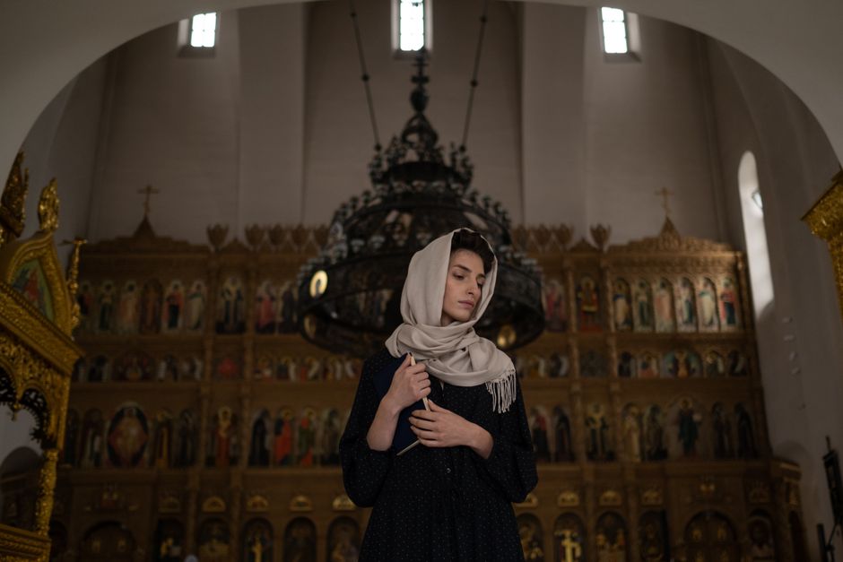 A woman wearing a headscarf and long skirt respectfully entering a historic Georgian Orthodox church.
