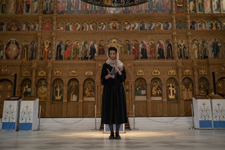 Woman In Beige Shawl On Head Standing With Back To Altar And Holding Prayer Book