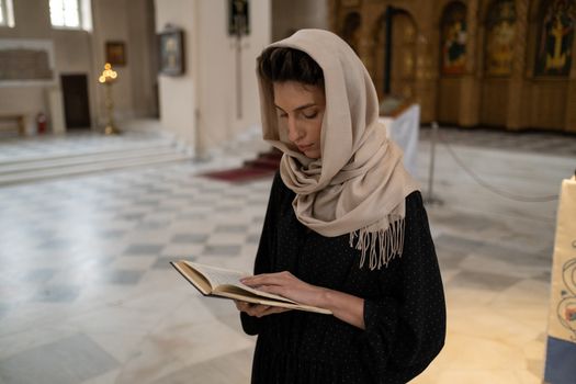 A woman wearing a shawl reads a book inside a church, embodying calm reflection.