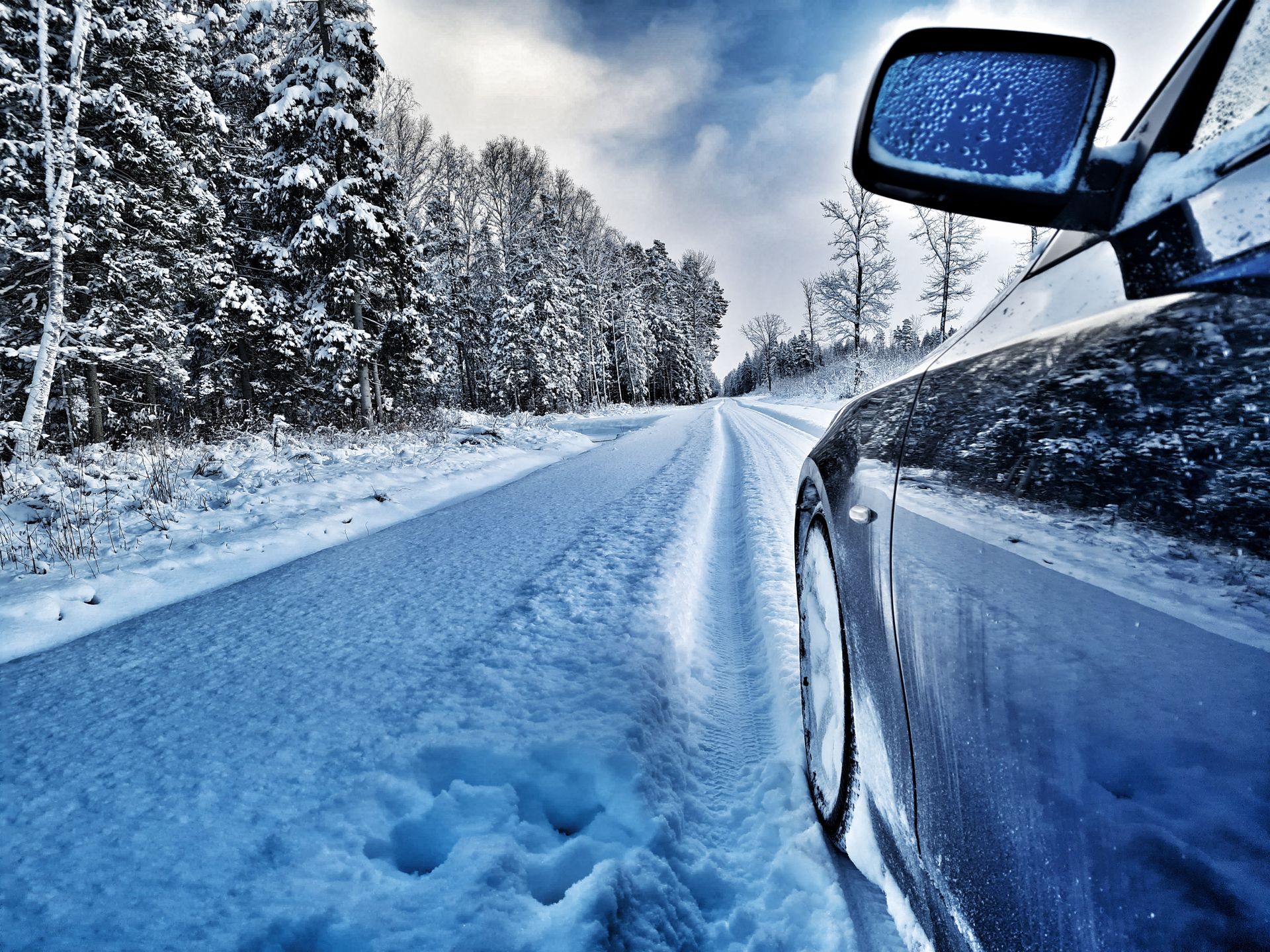 Fahrzeug fährt auf einer verschneiten Straße durch eine Winterlandschaft.