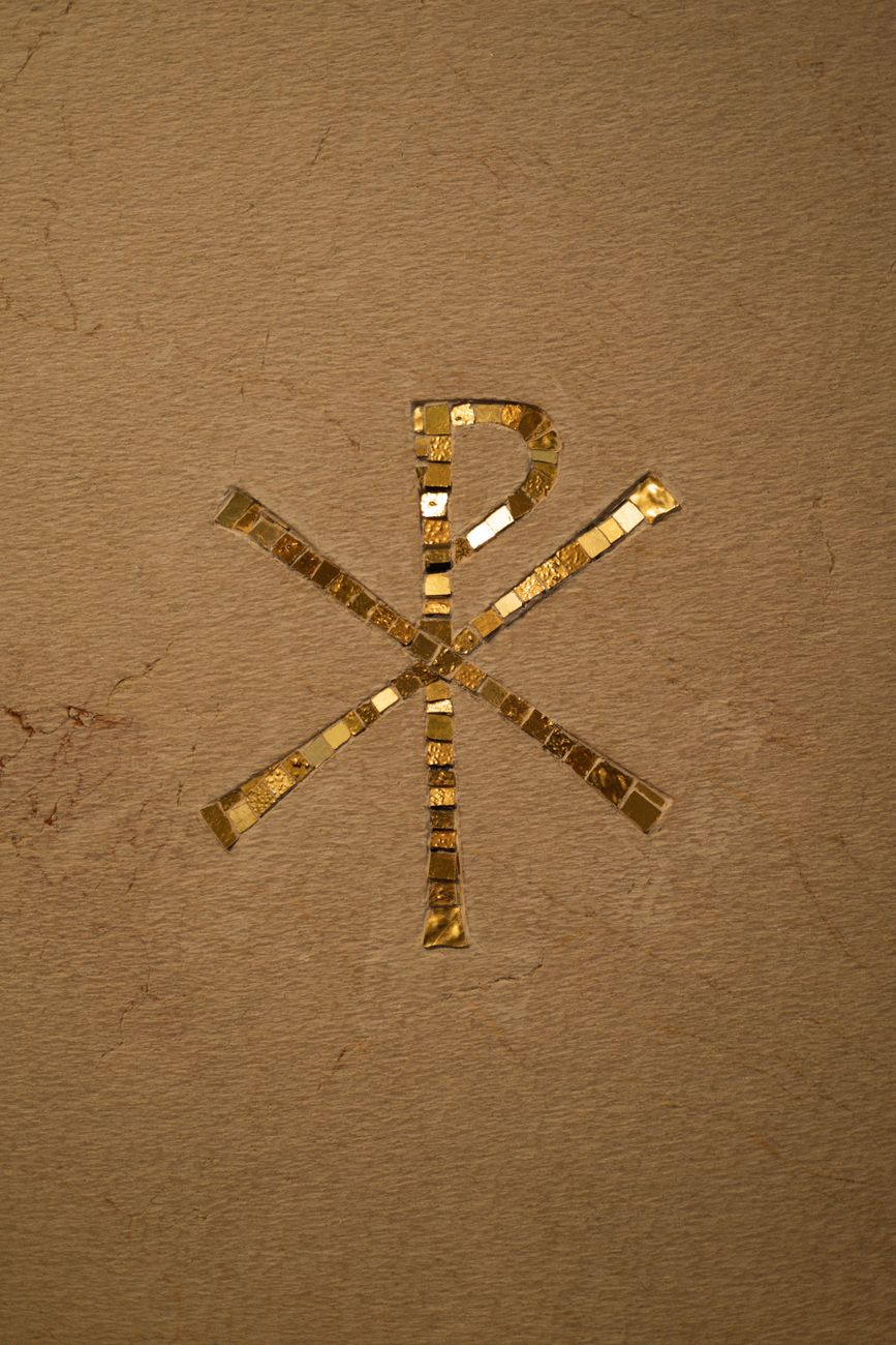 Intricate golden circular symbol rendered in ancient mosaic tiles on a textured stone background
