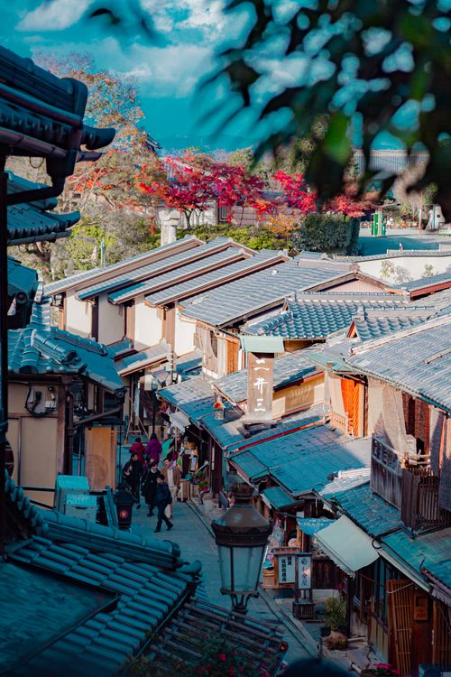 Free Explore a picturesque alley in Kyoto with traditional wooden buildings and vibrant autumn foliage. Stock Photo