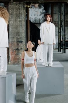 Stylish Asian women in modern white outfits standing on platforms, showcasing contemporary fashion indoors.